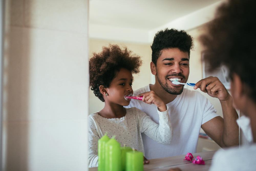 Black dad and black daughter brushing teeth together in mirror, wilmington de
