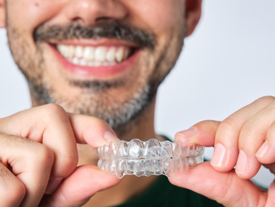 Man smiling holding invisalign clear aligners, wilmington de
